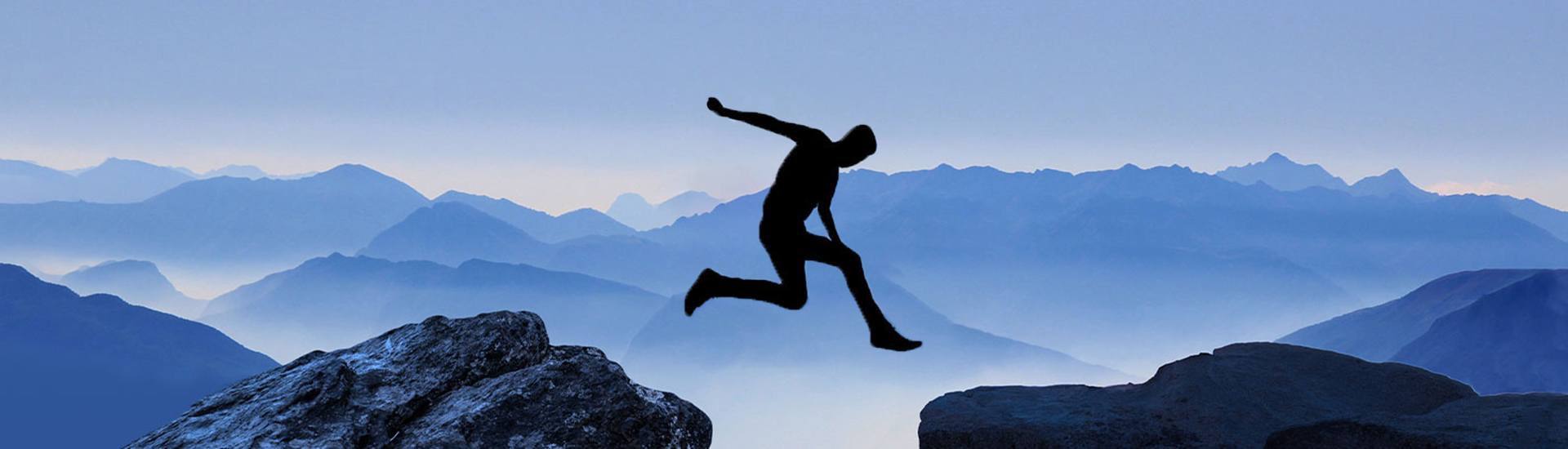 Foto einer Silhouette, die vor einem Bergpanorama über eine Kluft springt
