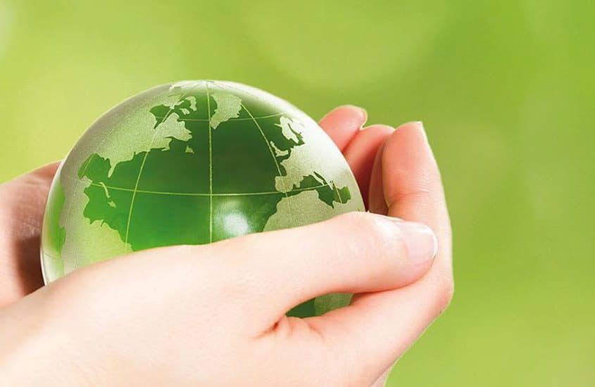 Hände halten eine grüne Glaskugel-Erde